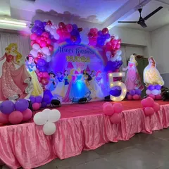 A grand stage for a 5th birthday, fit for royalty. This Disney Princess theme features a full lineup of princesses against a castle backdrop, framed by a beautiful balloon arch in shades of pink, purple, and white.