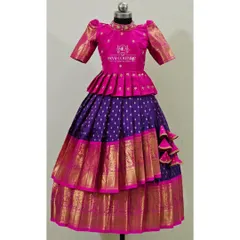 A stunning tiered pattu lehenga in pink and purple. The pink peplum top has delicate butti work, and the skirt features two layers of purple silk with wide Kanchi-style borders.