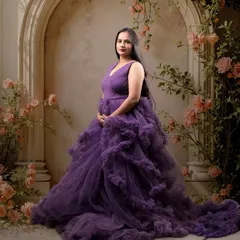 An elegant mom-to-be in a dramatic purple ruffled gown. The vintage-style floral backdrop adds a touch of classic romance to this maternity portrait.