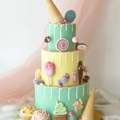 A three-tiered candy-land dream cake. This pastel creation is covered in a white chocolate drip and adorned with fondant ice cream cones, lollipops, candies, and macarons.