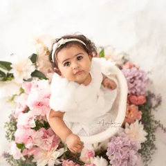 A beautiful sitter session portrait, with the baby looking up from a basket adorned with a ring of fresh flowers. The high-key lighting and floral elements create a soft, angelic look.