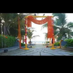 A vibrant entrance arch for a beachside wedding ceremony. The structure is decorated with bright orange marigold garlands, perfectly contrasting with the blue sky and surrounding palm trees.