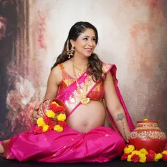 A vibrant and celebratory maternity portrait in a bright pink saree. The traditional jewelry and floral props beautifully complement this 'godh bharai' style shoot, capturing pure joy.