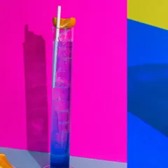 A vibrant purple and blue cocktail in a tall science beaker-style glass, using color blocking to create a playful and electric vibe.