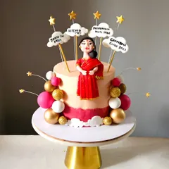 For a mother's 65th birthday, I created this elegant cake featuring a custom figurine in a red saree. The clouds above her mark key milestones in her life, making it a deeply personal and celebratory piece.