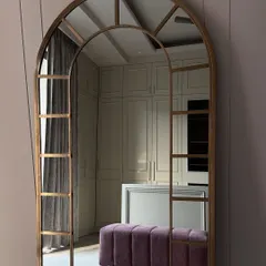 A glimpse into a walk-in closet that redefines personal luxury. This space features custom off-white cabinetry, a central island, a plush purple bench for seating, and a statement arched mirror, creating a functional and elegant dressing area.