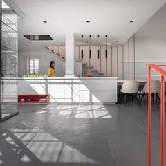 The open-plan kitchen and dining area is designed for connection. The long dining table extends from the kitchen island, creating a central hub for cooking, eating, and socializing, all while being bathed in natural light from the adjacent courtyard.