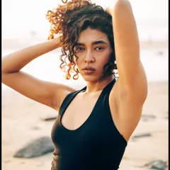 This outdoor beach portrait focuses on the model's natural beauty and curly hair texture. The soft, diffused light of the late afternoon is flattering and gentle, creating a relaxed and effortless vibe.