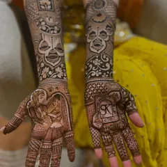 This design beautifully captures a tender wedding moment, the Varmala ceremony, on the bride's palm. On the other hand, we have the couple's initials, 'SK', enclosed in a traditional frame.