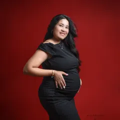 A classic and chic portrait. A simple, well-fitting black dress against a bold red background is a timeless choice for a maternity shoot.