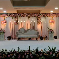 I designed this elegant engagement stage for an indoor hall. The setup features a classic white chaise lounge, a backdrop of warm candle-style lights, and a full floral border, creating a romantic and sophisticated look.