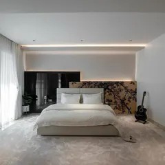 This master bedroom is a study in serene sophistication. A custom laser-cut headboard, plush carpeting, and soft, indirect lighting create a tranquil and inviting atmosphere, with a guitar in the corner adding a personal touch.