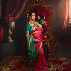 Reflecting on the journey ahead. This portrait, set in a room with regal, vintage decor, captures a moment of quiet contemplation, with the rich pink and green Kanjivaram saree adding a touch of royal elegance.