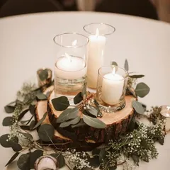 A rustic-chic centerpiece featuring candles in glass holders placed on a slice of a tree trunk, surrounded by eucalyptus leaves and baby's breath.