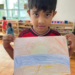 A child proudly displays his drawing of a sunrise. Art is a powerful way for children to represent their understanding of the world and express their feelings.
