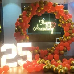 A balloon decoration for a 25th anniversary celebration at home. This setup combines a red and gold balloon arch with large light-up marquee numbers, creating a festive and memorable photo spot.