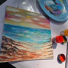 A student's finished seascape painting, with the art supplies used sitting alongside it. Our studio provides a relaxed space where you can unwind and create at your own pace.