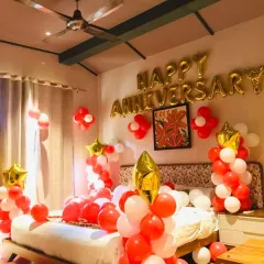 A romantic anniversary room setup with red and white balloons, 'HAPPY ANNIVERSARY' foil letters, and star-shaped foils.