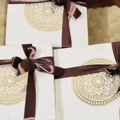 A trio of elegant white gift boxes with a gold mandala design, tied with a luxurious brown satin ribbon.