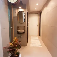 This passage connects the different rooms of the house, and we made sure it was bright and classy. The design includes a floating washbasin, an elegant oval mirror, warm overhead lighting, and a large wall clock as a statement piece.