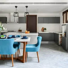 A look at a dining and kitchen area we designed for a private residence. We specialize in creating open-concept layouts where spaces flow seamlessly, like this kitchen that opens into a dining area defined by vibrant blue chairs and sleek pendant lights.