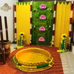 A vibrant Haldi ceremony decoration with a backdrop of banana leaves and marigold flowers, featuring traditional elements like a brass urli for the ceremony.