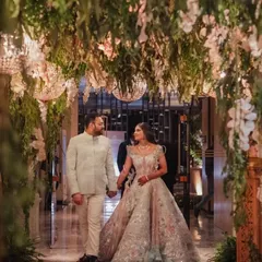 A fairytale couple entrance. The walkway is designed as an enchanted tunnel with hanging foliage, white orchids, and sparkling chandeliers, creating a romantic and magical moment.