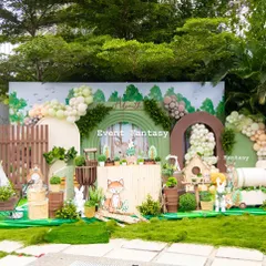 A full view of Advaith's woodland party setup. This expansive outdoor decoration includes a detailed backdrop with a forest scene, a rustic wooden fence, and adorable animal characters scattered throughout the grassy area.