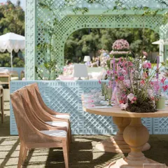A seating area at the 'Mayfair Luncheon', with a backdrop of pastel blue trellis structures. The combination of natural wood chairs and soft colors created a light and loving mood.