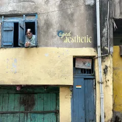 An 'aged aesthetic' indeed. An elderly man looks out from his window with its bright blue shutters, above a weathered green and blue facade.