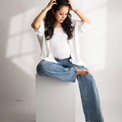 A relaxed and stylish pose. This mom-to-be looks effortlessly cool in her jeans and white shirt, seated on a white block.