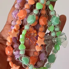 A handful of happiness. This shot shows the collection of pastel beaded keychains in purple, orange, and green, each adorned with cute heart, star, and butterfly beads.