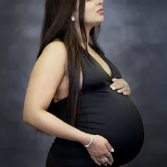 A serene and graceful side-profile portrait. This pose beautifully highlights the baby bump and captures a moment of quiet reflection for the mom-to-be, set against a classic dark studio backdrop.