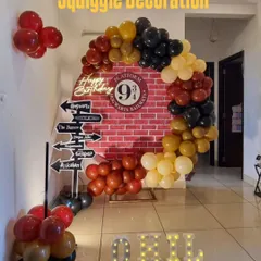An intimate at-home Harry Potter party setup, featuring a circular brick backdrop with a balloon garland and directional signs to iconic wizarding world locations.