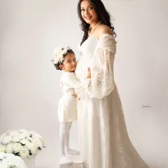 An angelic family portrait in all white. The older sister stands on a block to give her mom's baby bump a sweet hug.