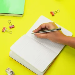 A hand is captured writing in a notebook against a vibrant yellow background. This action shot brings the product to life and highlights its use in a fun, creative context.