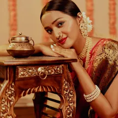 A close-up portrait of a woman in a traditional red saree, resting her head on a carved wooden table, creating a moment of quiet reflection amidst the festivities.