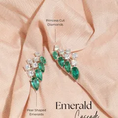 A product shot of the Emerald Cascade earrings against a soft fabric. This view highlights the beautiful contrast between the geometric princess cut diamonds and the organic shape of the pear cut emeralds.