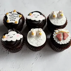 These custom fondant cupcakes tell a sweet story for a mom-to-be. The set includes various designs like sleeping clouds and tiny baby shoes, all part of a "Twinkle Twinkle Little Star" theme.