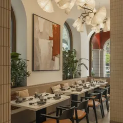 The main dining area features clean lines, a custom fan-like chandelier, and large abstract art. The space feels open and serene, with plenty of natural light from the arched windows.