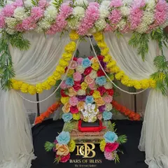 A vibrant and colorful floral backdrop for Ganesh Chaturthi. This unique design features a wall of multi-colored flowers behind the idol, framed by pink and white floral arrangements and yellow marigold garlands.