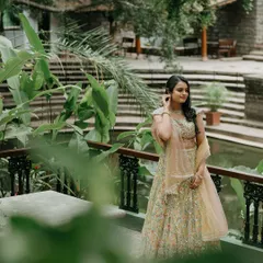 A bride in a light green lehenga stands by the pond, the natural setting enhancing her beauty.