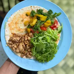 A deconstructed chicken wrap on a whole grain tortilla, loaded with fresh greens, bell peppers, and seasoned chicken. A perfect DIY high-protein meal.