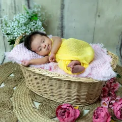 A little ray of sunshine. This newborn is sleeping so peacefully in a cozy basket, dressed in a bright yellow outfit that matches her sunny disposition.