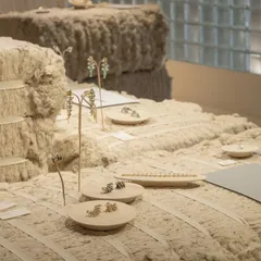 A close-up of the jewelry display on the raw cotton bales. The soft, organic texture of the cotton provides a beautiful backdrop for the metallic forms of the jewelry, highlighting their precision and craft.