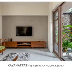 This view from the living room at Kayanattath House shows the seamless transition to the courtyard through large sliding glass doors, which feature a stone wall and a vibrant red jali screen.