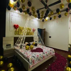 An intimate birthday room surprise shown in evening light. The combination of gold and black balloons, a fairy light canopy, and a rose petal path creates a warm and celebratory atmosphere.