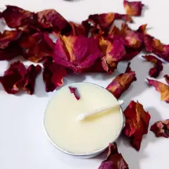 A close-up of a single tealight, showing how a delicate rose petal is embedded in the creamy soy wax.
