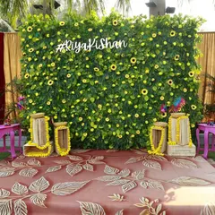 A custom photo wall for the Haldi ceremony. The lush green backdrop is dotted with sunflowers and features the couple's hashtag, creating a personalized and vibrant spot for pictures. The pink benches add a fun pop of color.