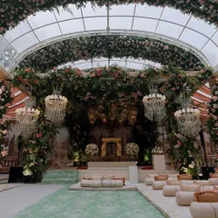 A wide view of the Anand Karaj ceremony space, showing the grand arched structure covered in flowers and greenery. The combination of floor seating on custom cushions and elegant chairs provides comfortable viewing for all guests.